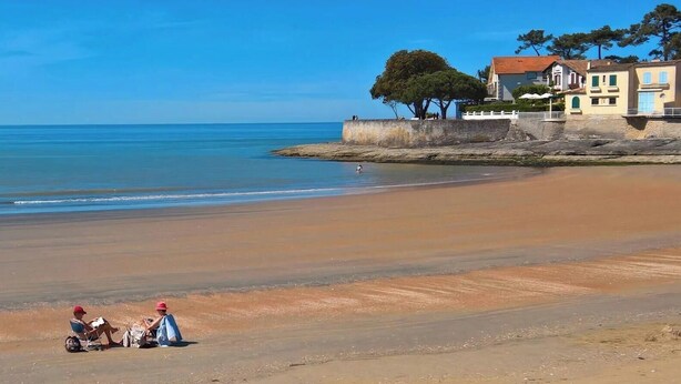 A beach with a clear sky, a sandy shore, and a building with a balcony overlooking the sea. - Apartment "Les Orphies" with Private Terrace, Shared Garden and Wi-Fi (Vaux-sur-Mer)