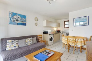 A compact living space with a sofa, dining table, kitchen area, and artwork on the walls. - Apartment "Les Orphies" with Private Terrace, Shared Garden and Wi-Fi (Vaux-sur-Mer)