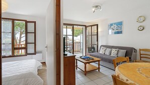 A room with a bed, a wooden table, a sofa, and a dining table with chairs. - Apartment "Les Orphies" with Private Terrace, Shared Garden and Wi-Fi (Vaux-sur-Mer)