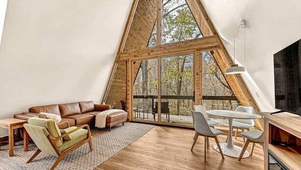 Et hyggeligt, trekantet soveværelse med loft, stort vindue, sofa, stol og lille bord.