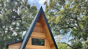 A wooden cabin with a triangular roof, a front door, and a small porch with steps leading up to it. - White Oak Haven-Cozy Forest A-frame near Bentonville (Benton County)