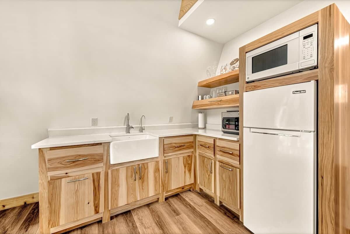 A modern kitchen with wooden cabinets, a white countertop, a sink, a microwave, and a refrigerator.