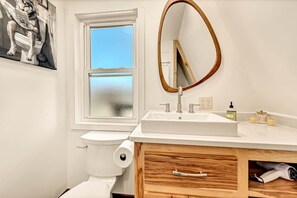 A modern bathroom with a toilet, a window, a sink, and a wooden vanity.