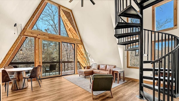 Um loft espaçoso com um amplo teto de madeira, uma escada espiral preta e vista para árvores através de grandes janelas.