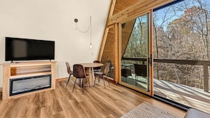 Um interior moderno com uma TV sobre um suporte de madeira, uma mesa de jantar com cadeiras e uma grande porta de vidro deslizante que dá para um deck ao ar livre.