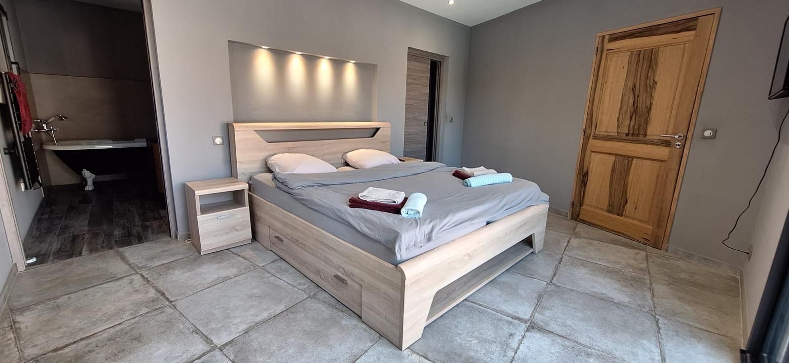 Une chambre à coucher avec un lit en bois, des tables de chevet, un banc intégré, une armoire en bois et une salle de bain avec une baignoire.