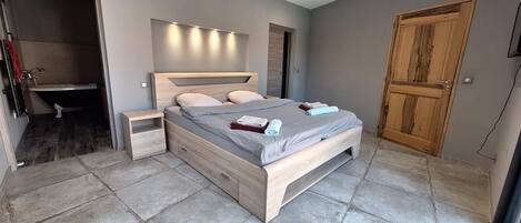 Une chambre à coucher avec un lit en bois, des tables de chevet, un banc intégré, une armoire en bois et une salle de bain avec une baignoire.
