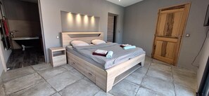 A bedroom with a wooden bed, bedside tables, a built-in bench, a wooden wardrobe, and a bathroom with a bathtub. - Modern villa with swimming pool (Vézénobres)
