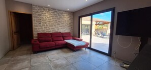 A living room with a red sofa, a stone wall, a sliding glass door to an outdoor area, and a television. - Modern villa with swimming pool (Vézénobres)