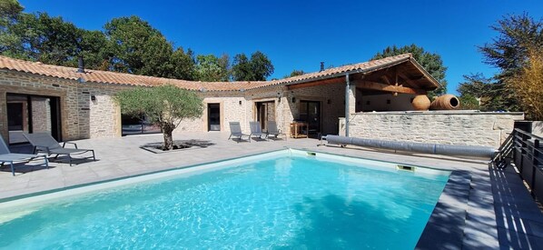 A poolside area with a stone building, lounge chairs, and a clear blue pool.