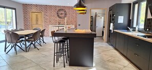 A modern kitchen with a central island, dark cabinetry, and a brick accent wall. - Modern villa with swimming pool (Vézénobres)