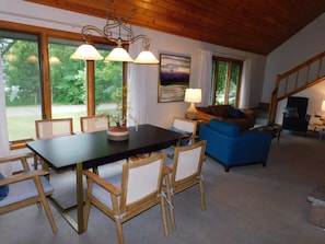 A cozy living room with a wooden ceiling, a dining table with chairs, a blue sofa, and a fireplace.