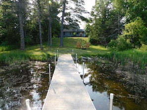 A concrete pathway leading to a house surrounded by trees and a small pond.