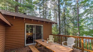 Una cabaña de madera con un porche, una mesa de picnic y dos sillas Adirondack.