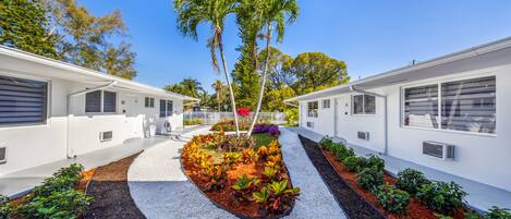 A modern building with a central garden area, surrounded by white walls and featuring palm trees and various plants.