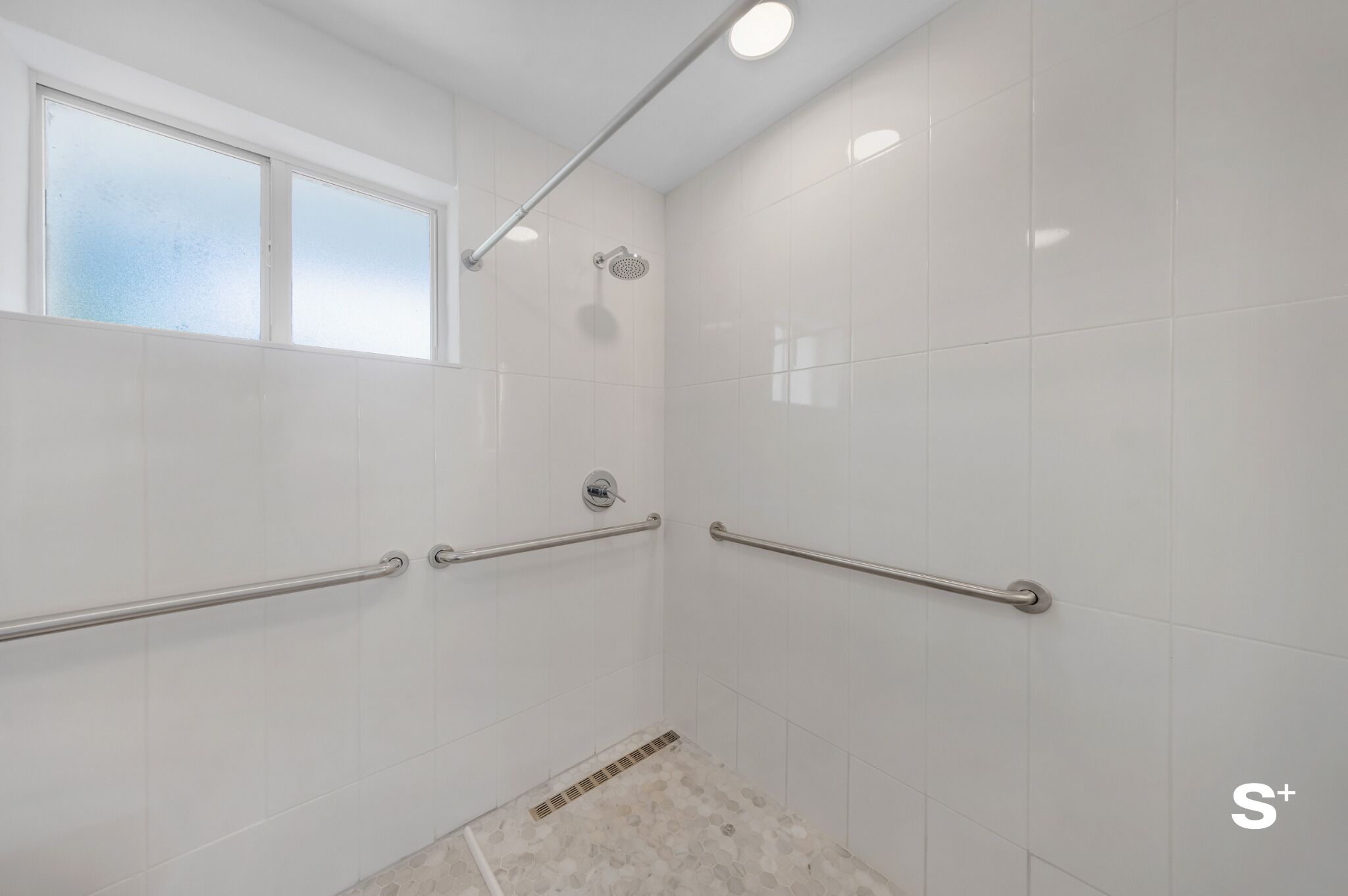 Un baño con azulejos blancos, una ventana, ducha y barras de apoyo.