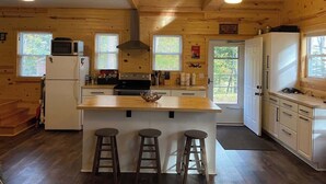 Cocina de cabaña de madera con una isla central, taburetes de bar, estufa y refrigerador.