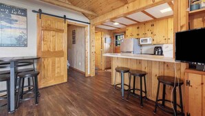 A wooden interior with a kitchen area, bar stools, and a television. - Lakefront Cabin: Dock, Bunkhouse, Pet-Friendly (Deerwood)