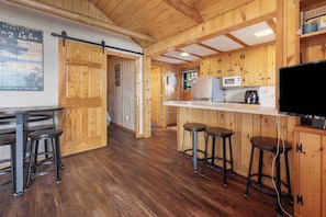Un interior de madera con zona de cocina, taburetes de bar y televisor.
