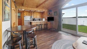 A wooden cabin with a kitchen, dining area, and a large sliding glass door leading to a lake view. - Lakefront Cabin: Dock, Bunkhouse, Pet-Friendly (Deerwood)