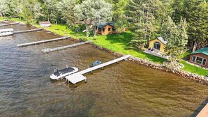 A lakeside property with docks, a small cabin, and a larger house surrounded by trees. - Lakefront Cabin: Dock, Bunkhouse, Pet-Friendly (Deerwood)