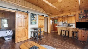 A cozy cabin interior with a wooden dining area, kitchen, and a large sliding door leading to a balcony. - Lakefront Cabin: Dock, Bunkhouse, Pet-Friendly (Deerwood)