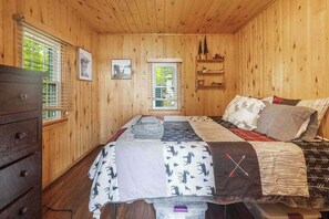 Une chambre à coucher dans une cabane en bois, avec un lit, une commode et deux fenêtres.