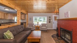 Una sala de estar acogedora con chimenea, techo de madera y una cocina visible al fondo.