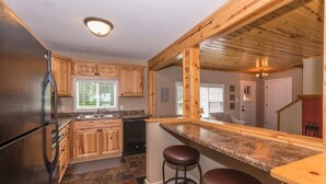 Cocina con armarios de madera, encimera de granito, refrigerador de acero inoxidable y barra con taburetes.