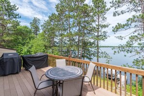A deck with a round table and chairs, overlooking a lake with trees. - Upper Hay Pet Friendly Getaway Home (Pequot Lakes)