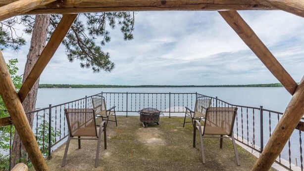 Una terraza de madera con cuatro sillas y un hogar para fuego, con vista a un lago tranquilo.