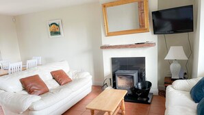 Ett vardagsrum med en vit soffa, ett soffbord i trä, en öppen spis, en tv och en matplats med stolar.