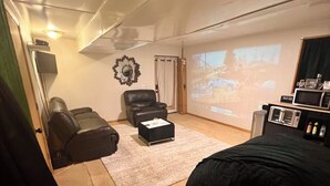 A compact living space with a large bed, a leather chair, a small table, a projector screen, and a microwave. - Homey and Relaxing Stay w/Private Movie Theater Room (Jonesboro)