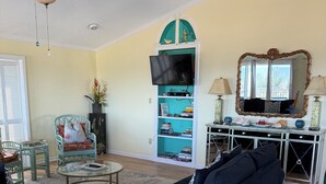 A living room with a sofa, a glass coffee table, a television on a stand, and a bookshelf. - Oceanfront Tybee Island, a spacious home perfect for family vacations. (Tybee Island)