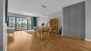 A spacious living room with a wooden floor, a dining area with a table and chairs, a bookshelf, and a large sliding door closet.