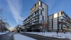 A multi-story residential building with balconies, a speed limit sign, and a snow-covered street.