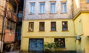 Un edificio de varios pisos con fachada amarilla, una puerta de garaje cerrada y un pequeño rosal en primer plano.