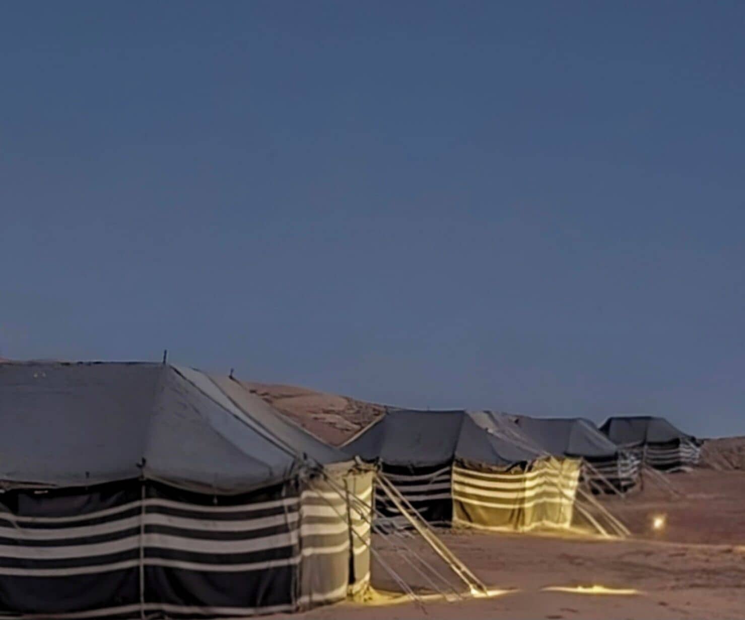 Une rangée de tentes dotées d’un toit plat et d’une auvent rayé, se dressant sur fond de paysage désertique.