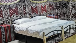 Una cama con estructura metálica, ropa de cama blanca y cortinas estampadas.