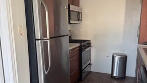 Une cuisine équipée d’appareils électroménagers en acier inoxydable, de meubles de rangement en bois, d’un four à micro-ondes, d’une cuisinière et d’une poubelle.