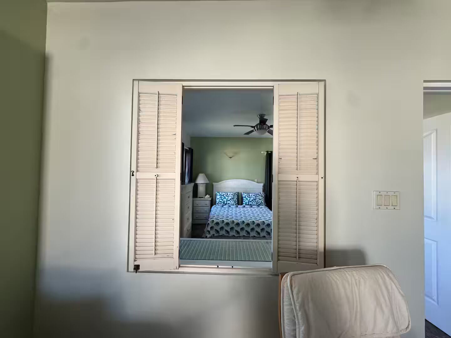 Quarto com cama, ventoinha no teto e janela com grades.