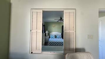 Quarto com cama, ventoinha no teto e janela com grades.