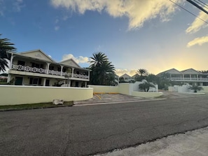 A two-story building with a balcony, surrounded by palm trees and a clear sky. - The Palms apt 1 (Cedar Grove)
