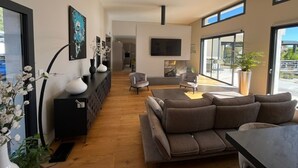 A modern living room with a sofa, a TV, and a fireplace. There is a large window and a door leading to another room. - Uzès, in a quiet, sought-after area, contemporary villa with swimming pool (Uzès)