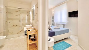 A modern bathroom with a glass shower enclosure, a sink, and a wooden shelf with towels. - Choir and Bentu Apartment  (Cagliari)