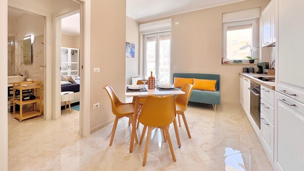 A modern kitchen with white cabinets, a dining area with a table and chairs, and a living area with a sofa. - Choir and Bentu Apartment  (Cagliari)