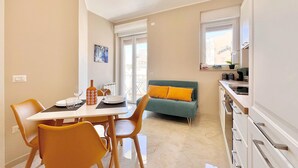 A dining area with a table, chairs, and a sofa in the background. - Choir and Bentu Apartment  (Cagliari)