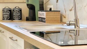 A modern kitchen with a glass countertop, stainless steel sink, and a coffee machine. - Choir and Bentu Apartment  (Cagliari)