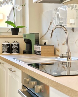 Eine moderne Küche mit Glasarbeitsplatte, Edelstahlspüle und einer Kaffeemaschine.