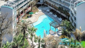 Ein Hotel mit einem zentral gelegenen Schwimmbad, umgeben von Liegestühlen und Palmen.